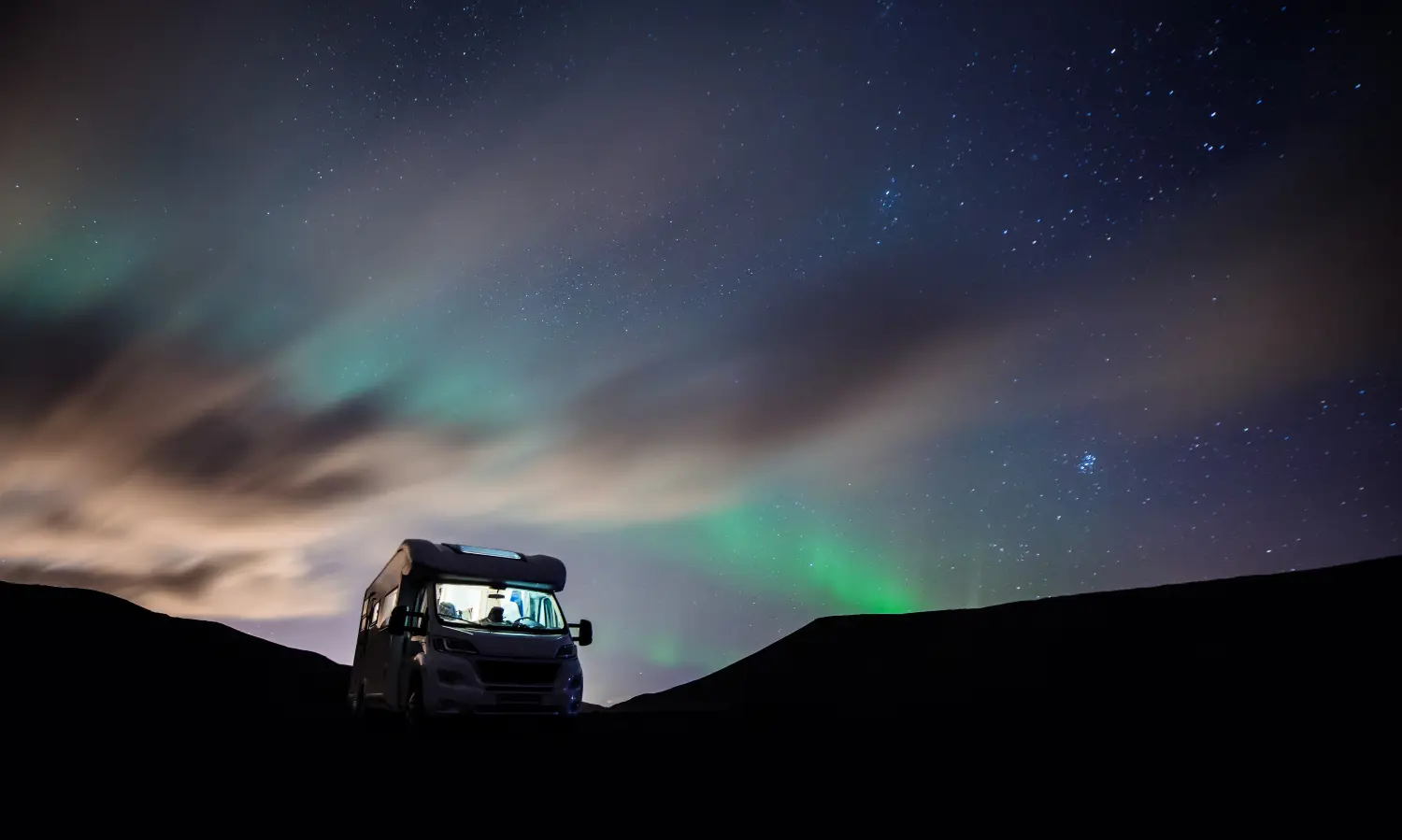 campervan parked on a hill next to the northern lights