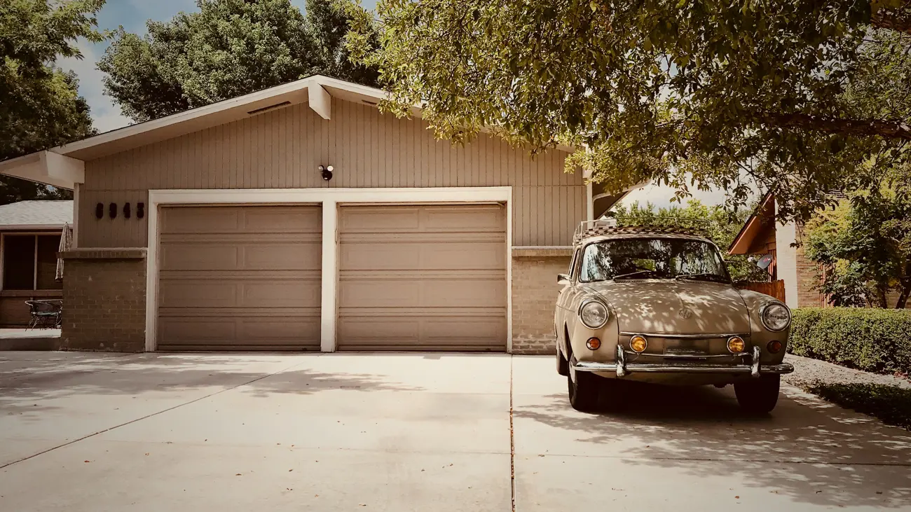 A classic car parked in-front of a driveway garage