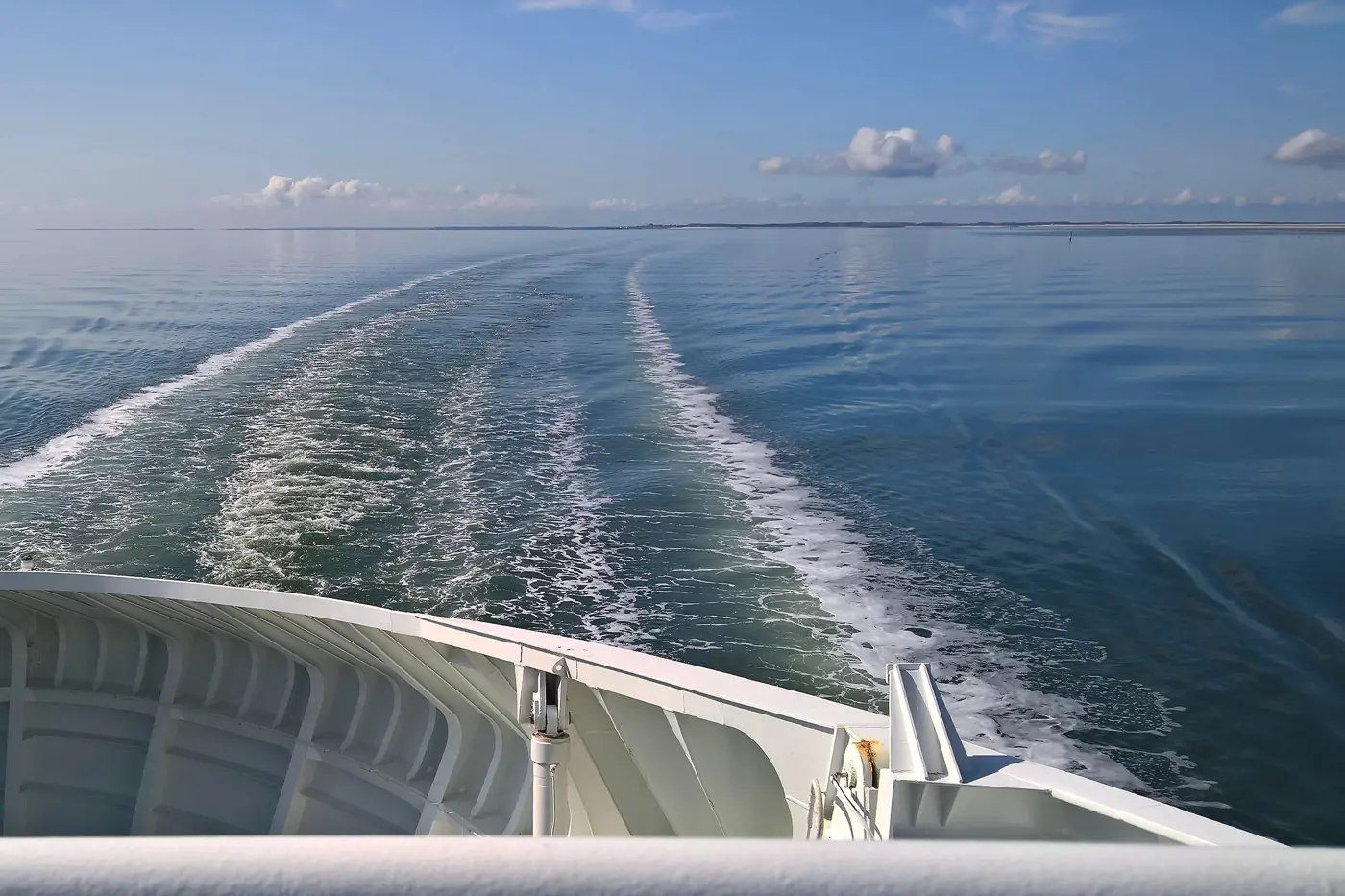 The rear of a ferry with its wake stretching across the sea into the distance