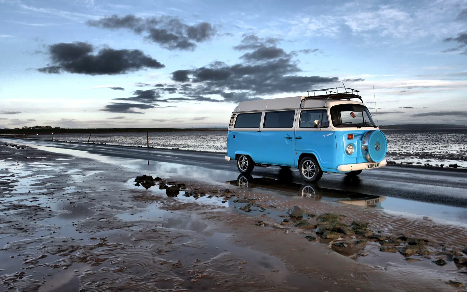 A blue campervan driving on a sandy beach