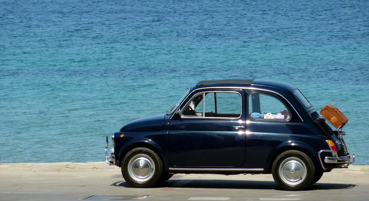 A black Fiat 500 parked in-front of the sea