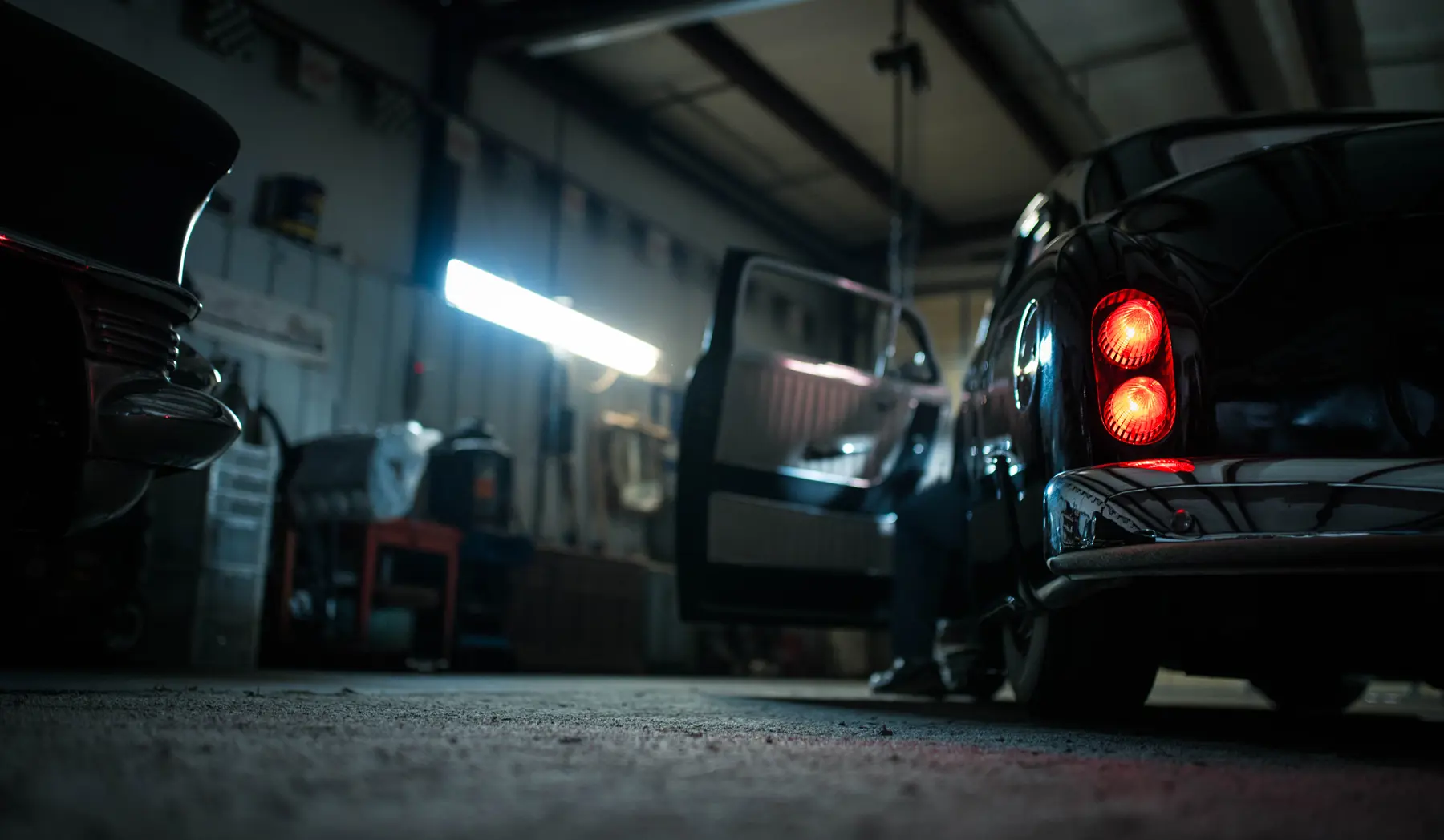 A classic car idling in a dimly lit garage with the owner working on restoring it