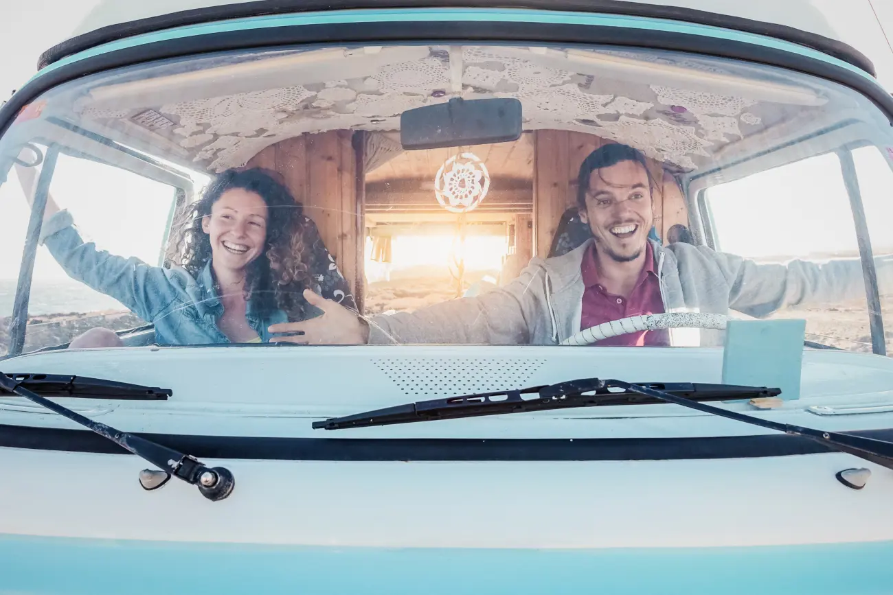 A couple sitting together inside the campervan with their arms stretched out