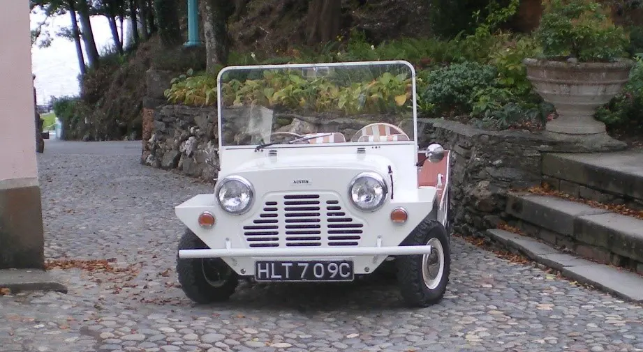A brown Mini Moke parked on the road side in a warm country