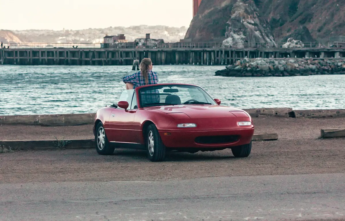 A red Mazda MX5 parked next to a mariner with the roof down