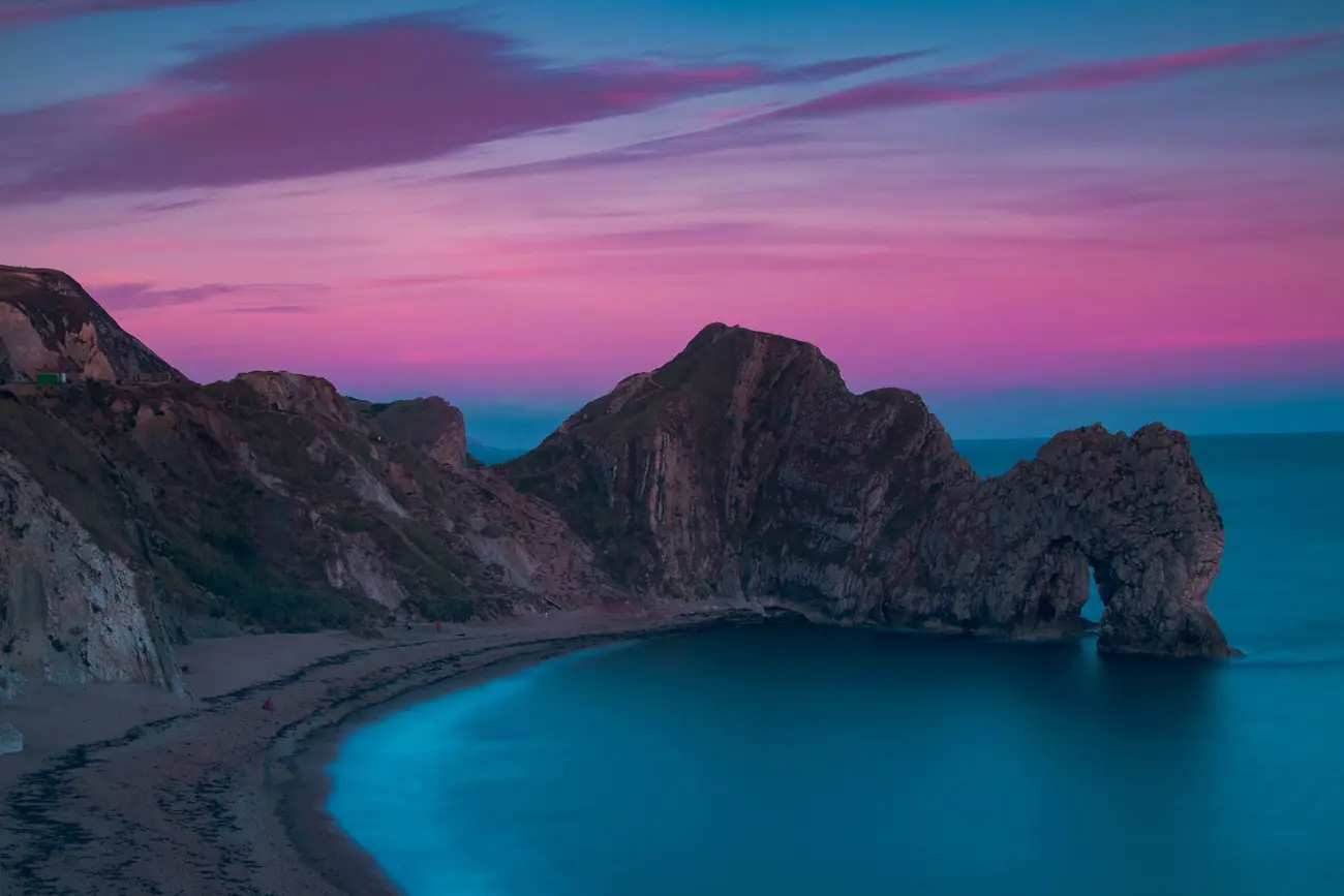 A large cliff with an arch stretching into the sea on a sandy beach at sunrise