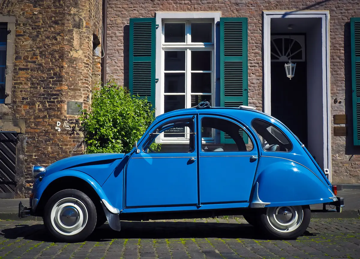 A classic blue Citroen 2CV parked in-front of a residential house