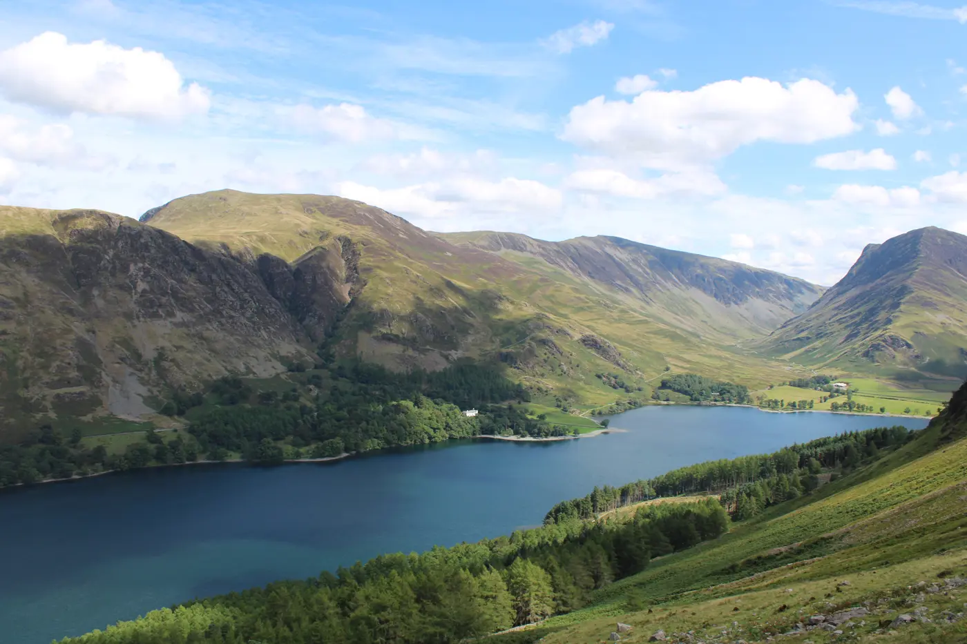 A scenic view across a large blue lake surrounded by woodland and rolling green hills