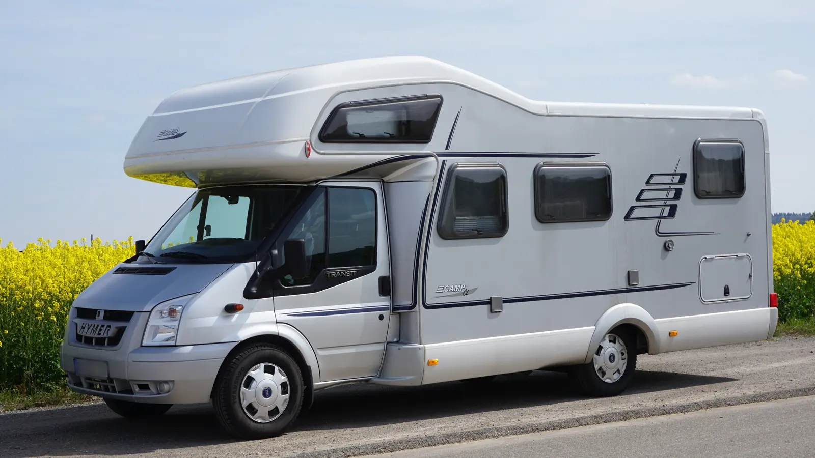 A grey motorhome parked out the side of a road with a field of large yellow crops behind it