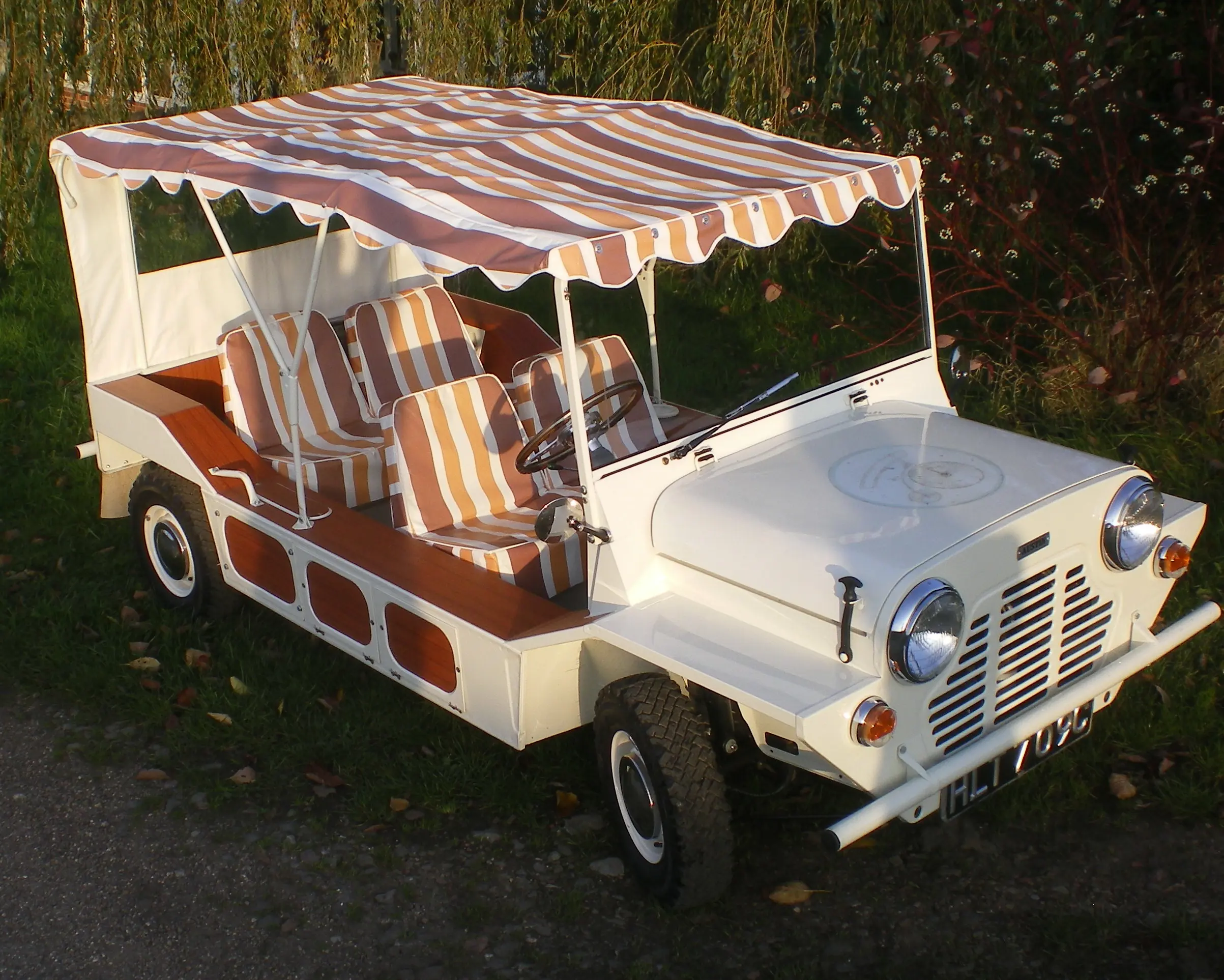 A white Mini Moke parked at the side of the road with a colourful fabric roof and interior