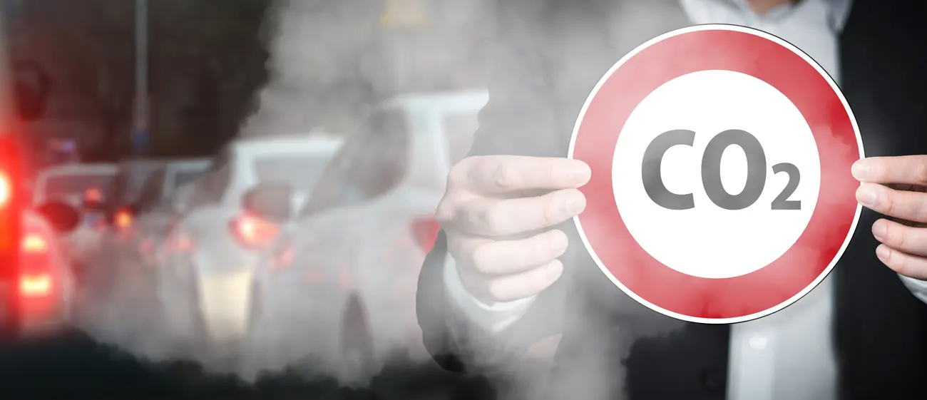 A man in a suit holding up a co2 warning sign in-front of a line of traffic
