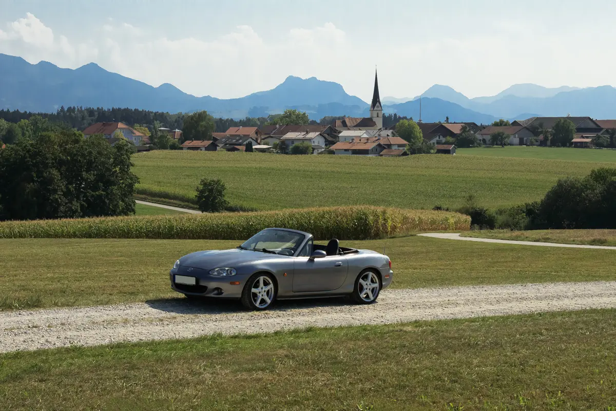 A classic Mazda MX-5 driving along a country road in a region of rural France