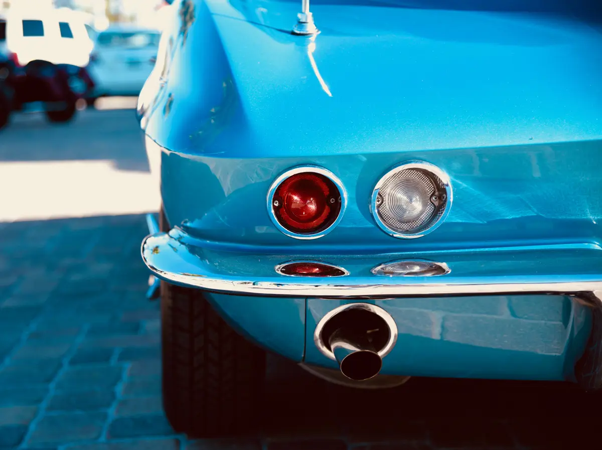 The rear near side corner of a classic teal car with the exhaust poking out