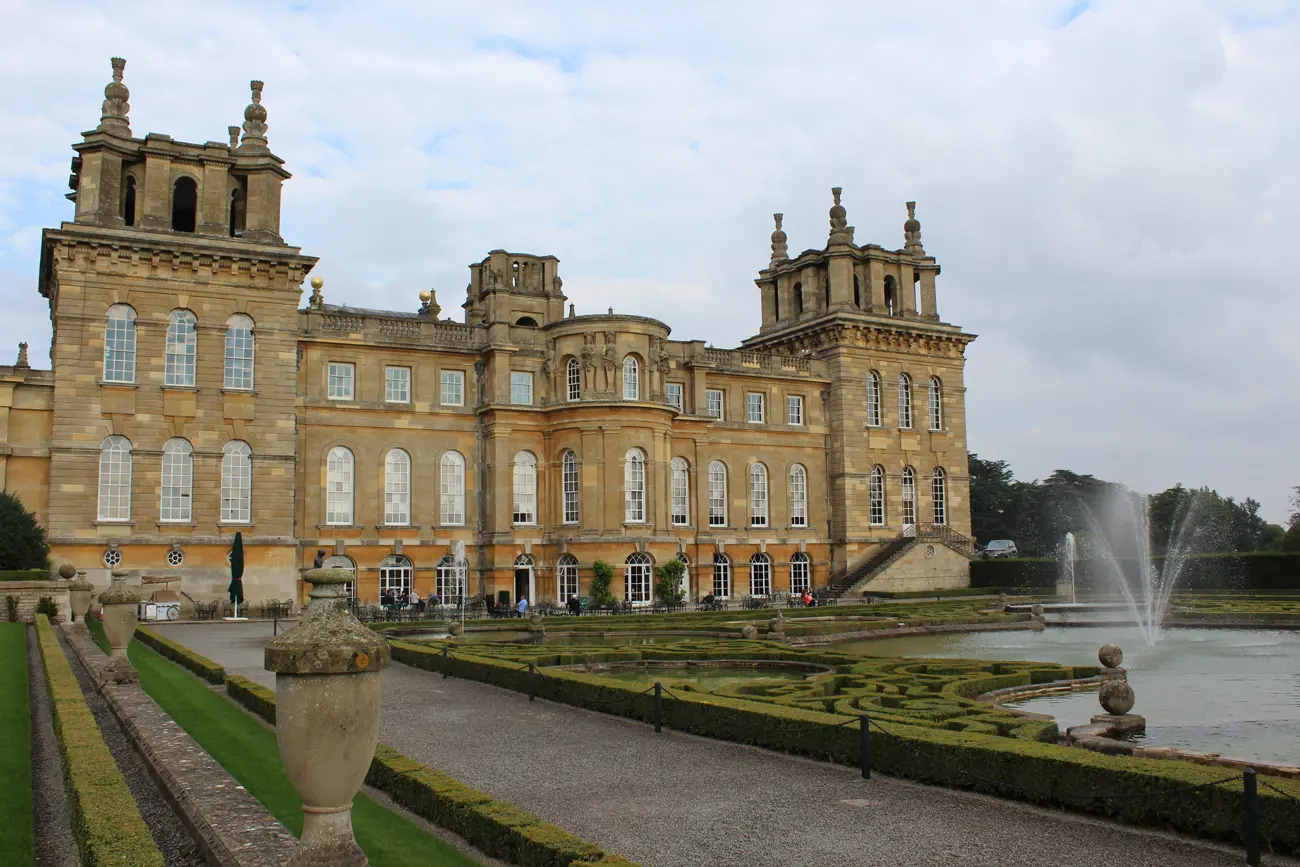 A large stone building with well kept gardens and a fountain in-front at Blenheim Palace