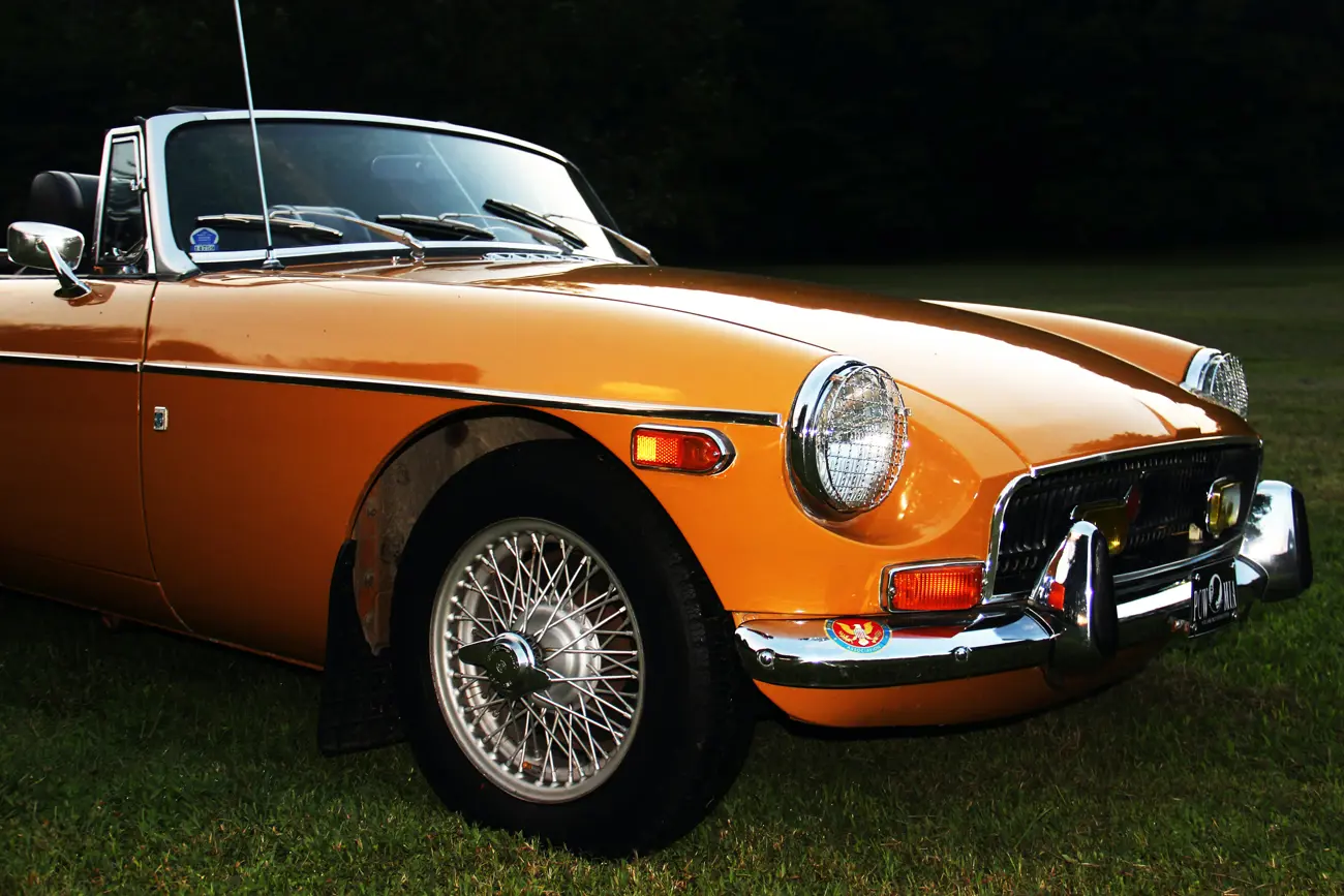 A classic orange MGB roadster parked in a field at dusk