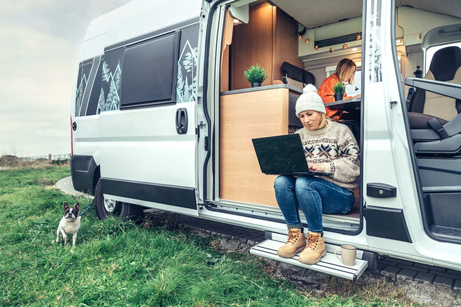 woman sat on the step of campervan with dog playing outside