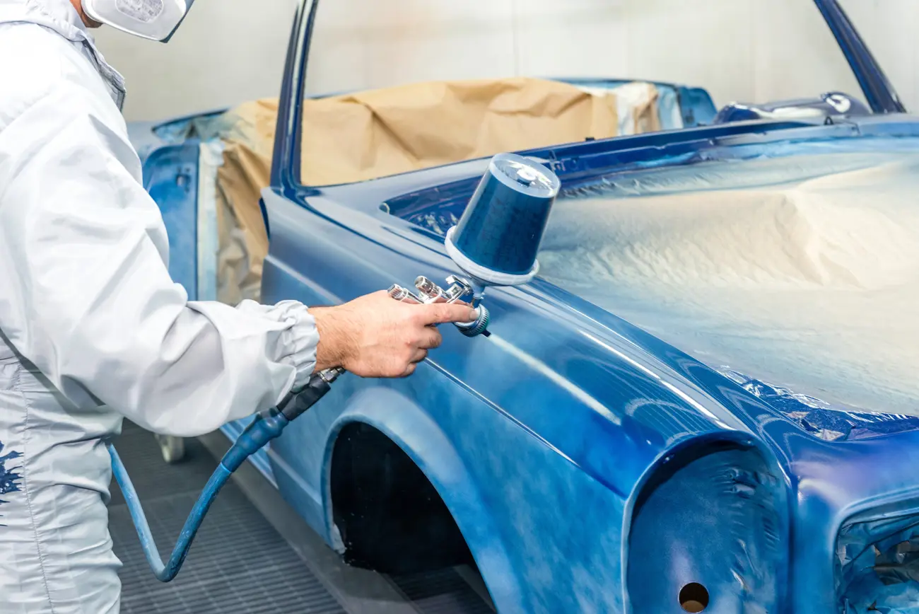 A man in protective clothing and a mask professionally spray painting a classic car shell