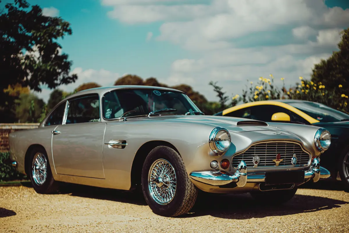 An Aston Martin DB5 parked in a gravel car park on a sunny day