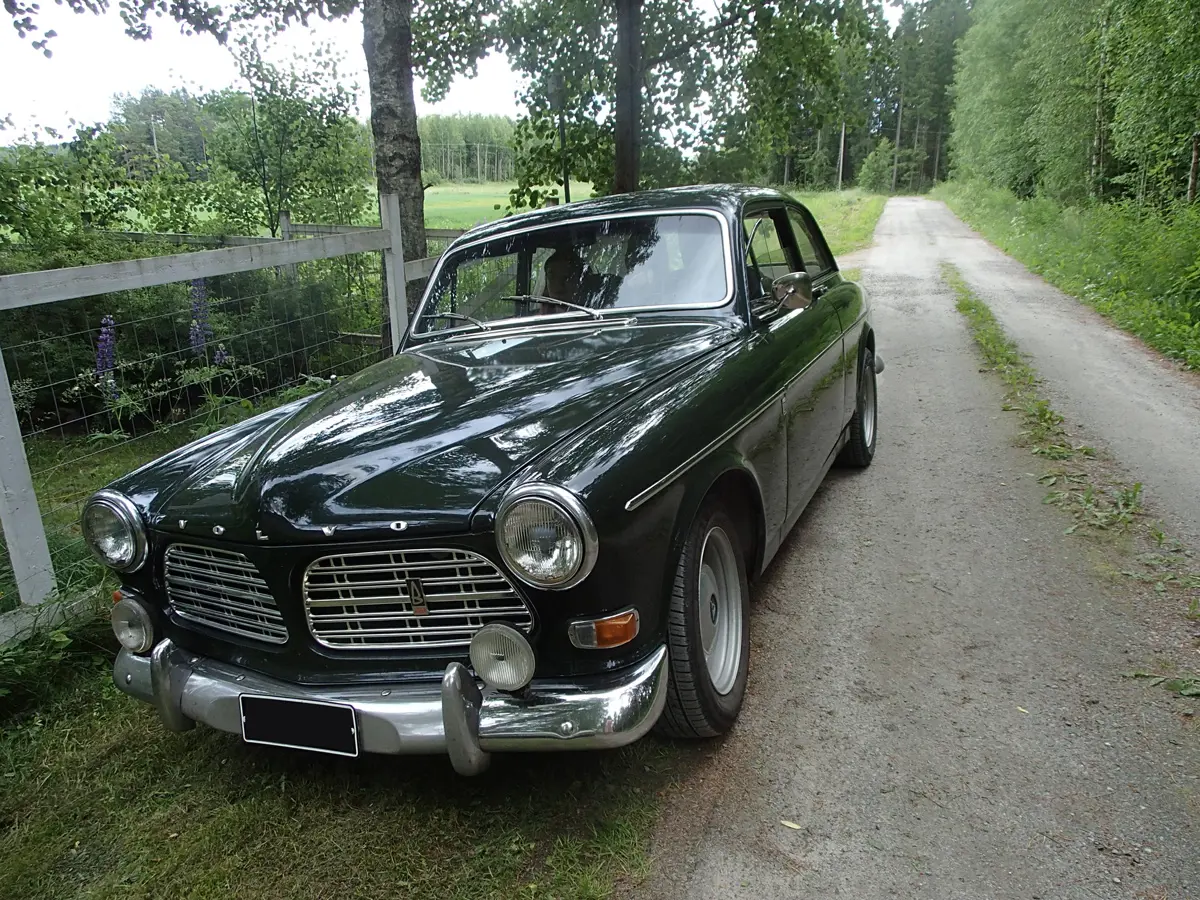 An early Volvo Amazon parked on the side of a country road with trees and hedges surrounding
