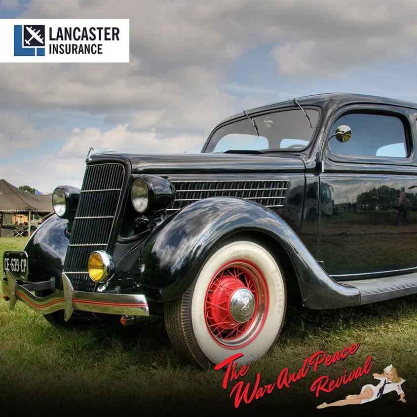 Black classic car with white wall tyres at show with Lancaster Insurance and The War and Peace Revival logos around it
