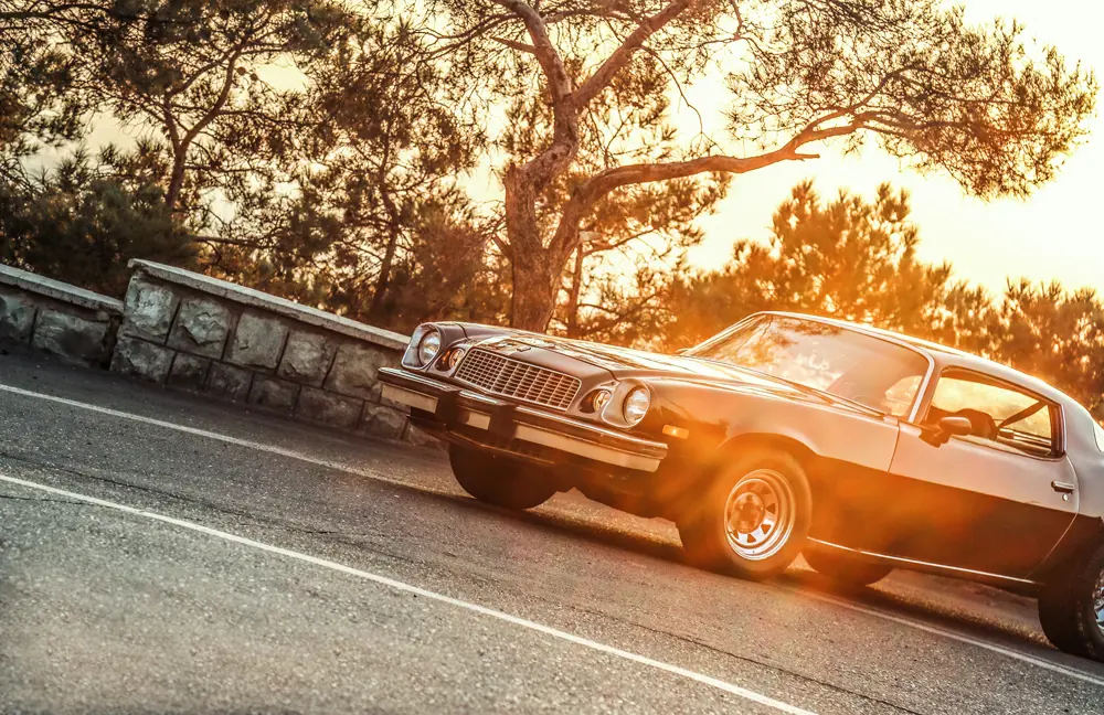 A classic American car parked with the sun setting behind it