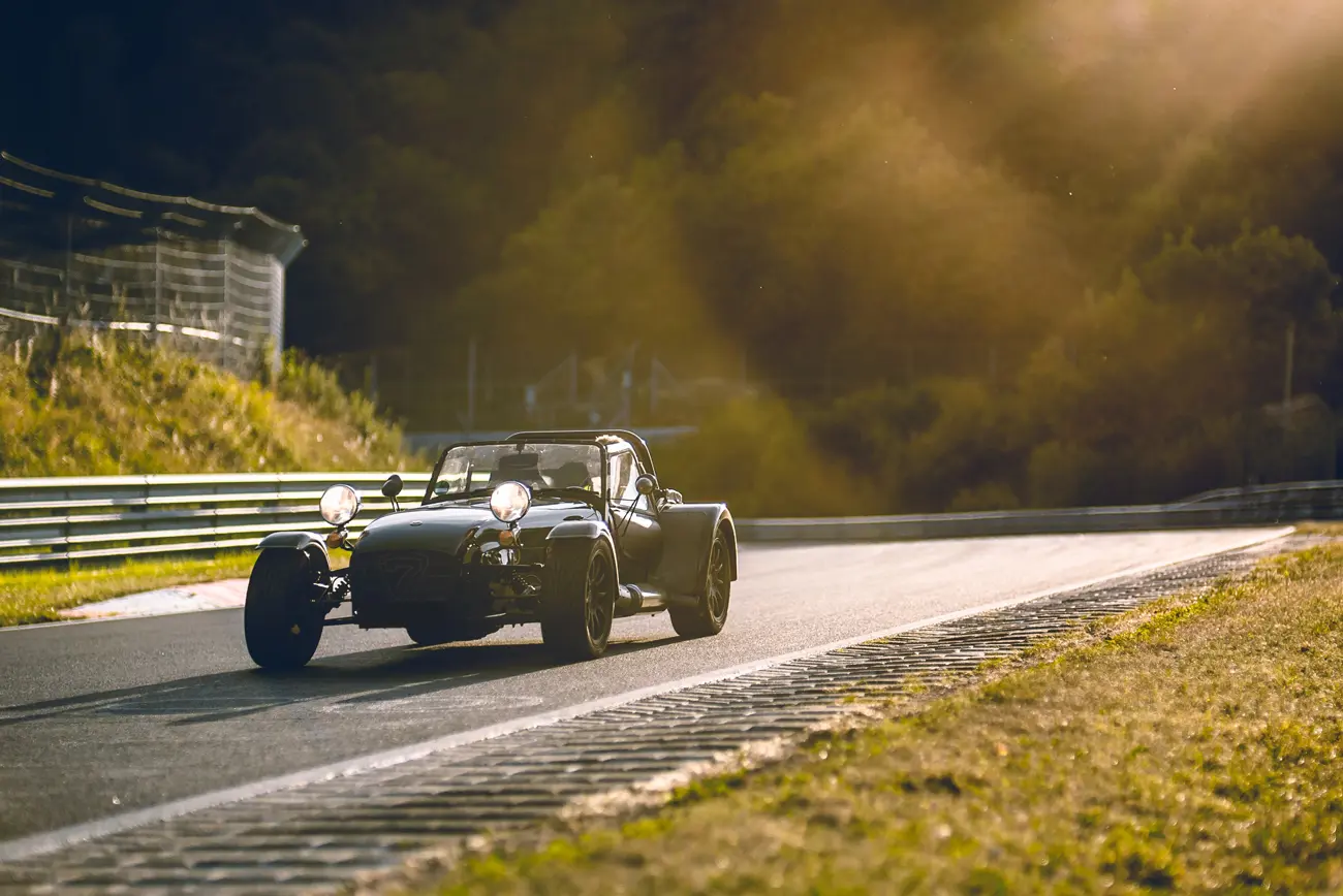 A classic car coming onto a straight on a race track with the sun setting behind