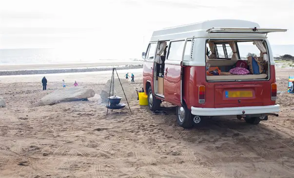 Red Volkswagen campervan set up on sandy beach