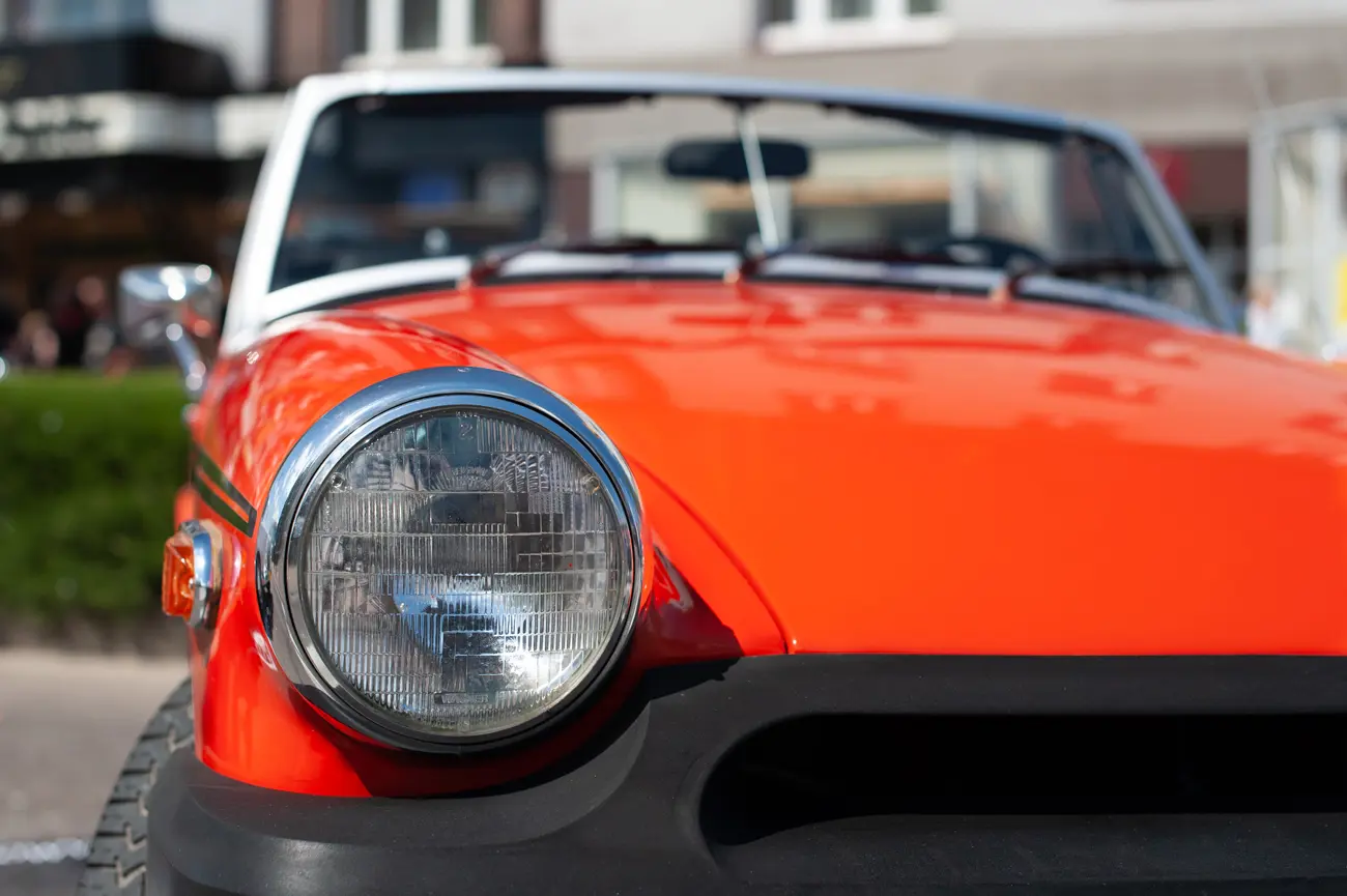 A front headlight of an MG Midget with a black rubber bumper