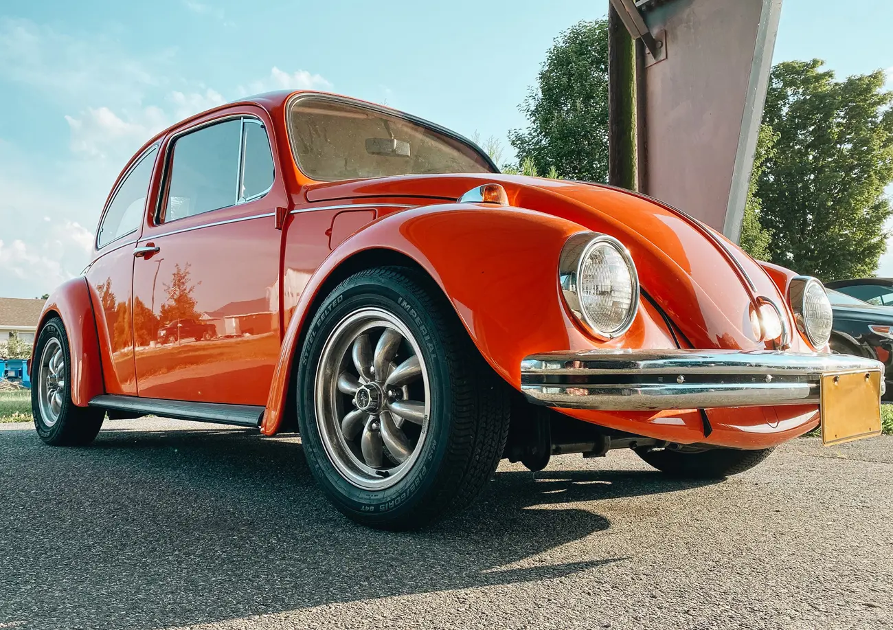 An orange classic VW Beetle parked in the sun