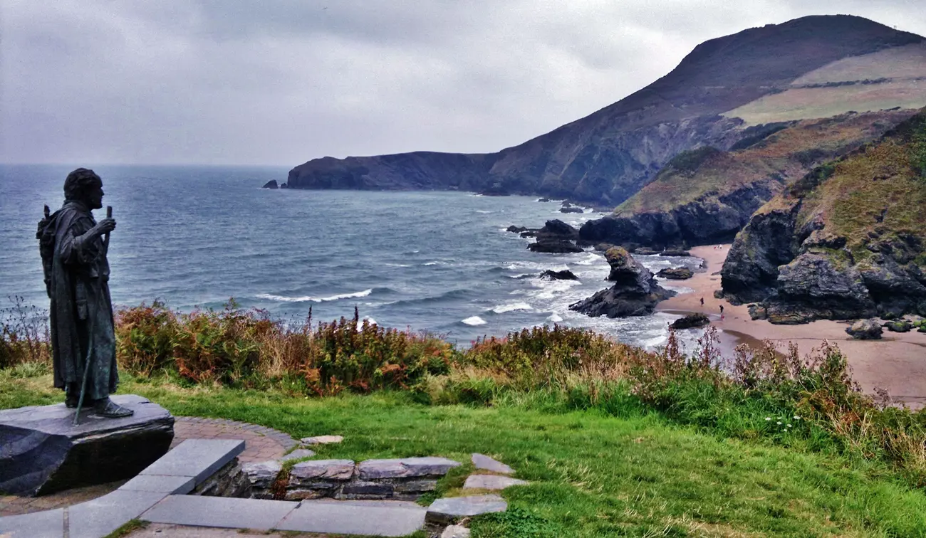 A statue on top of a headland looking over a rocky bay in Wales