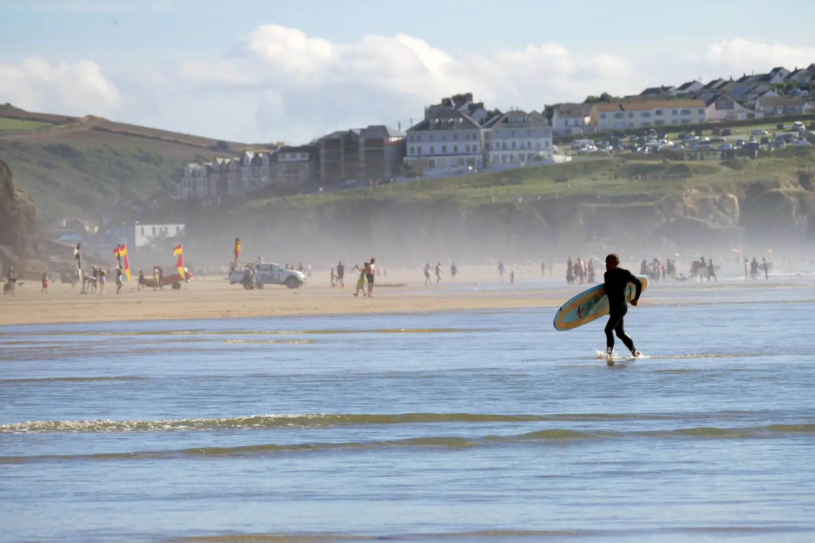 A person surfing on the sea in-front of a busy sandy beach in Cornwall