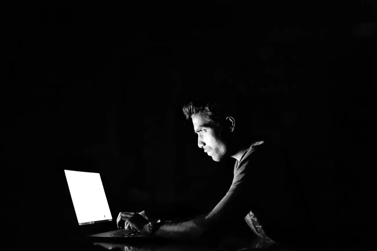 A scammer sitting in a dark room using a laptop