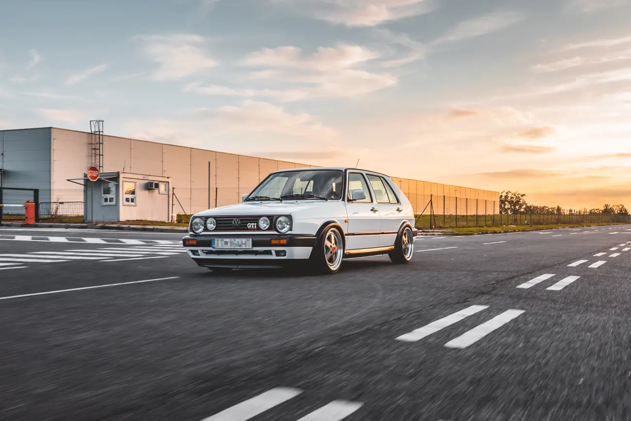 A classic Volkswagen Golf GTI driving fast on a road at sunset
