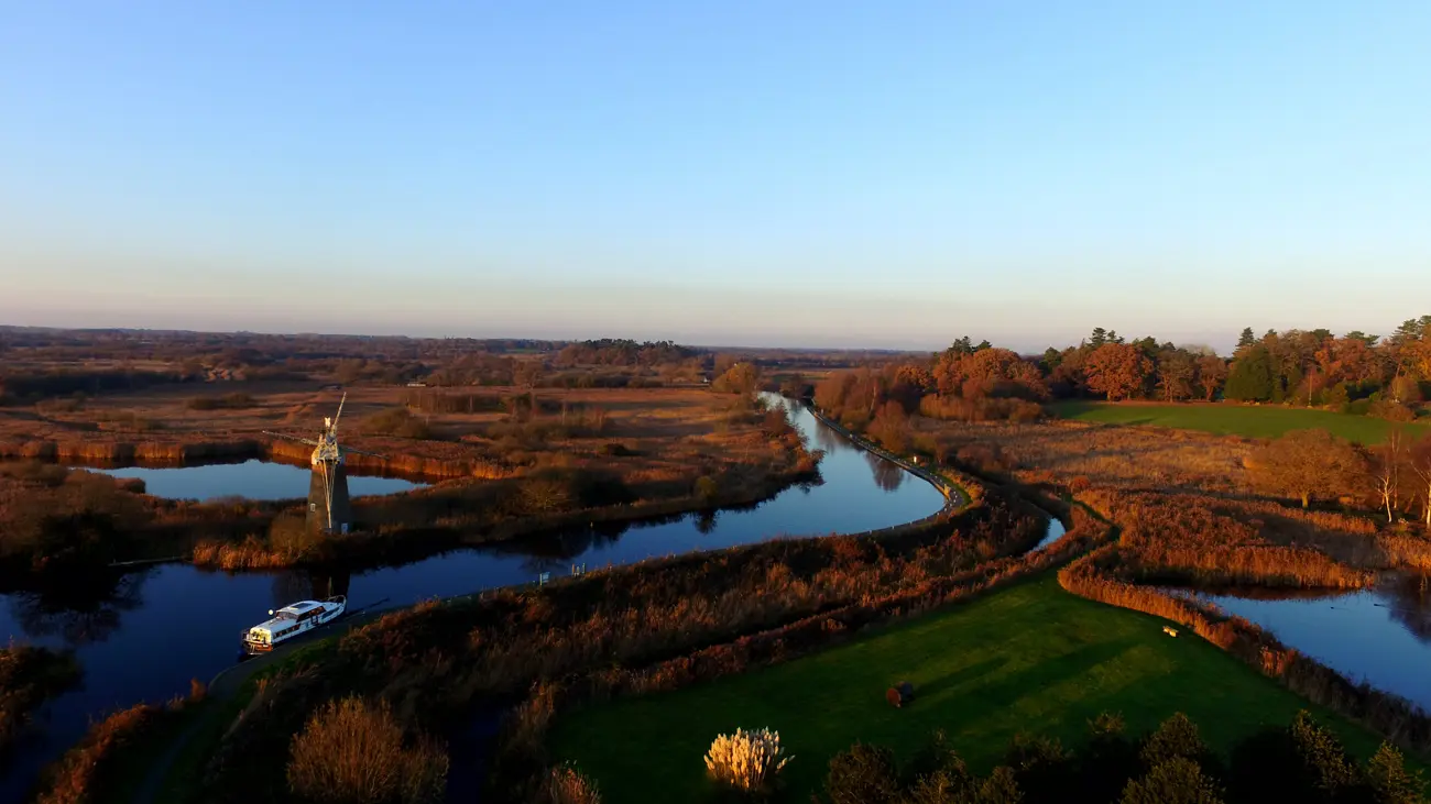 A view over the Norfolk Broads with a boat passing an old windmill