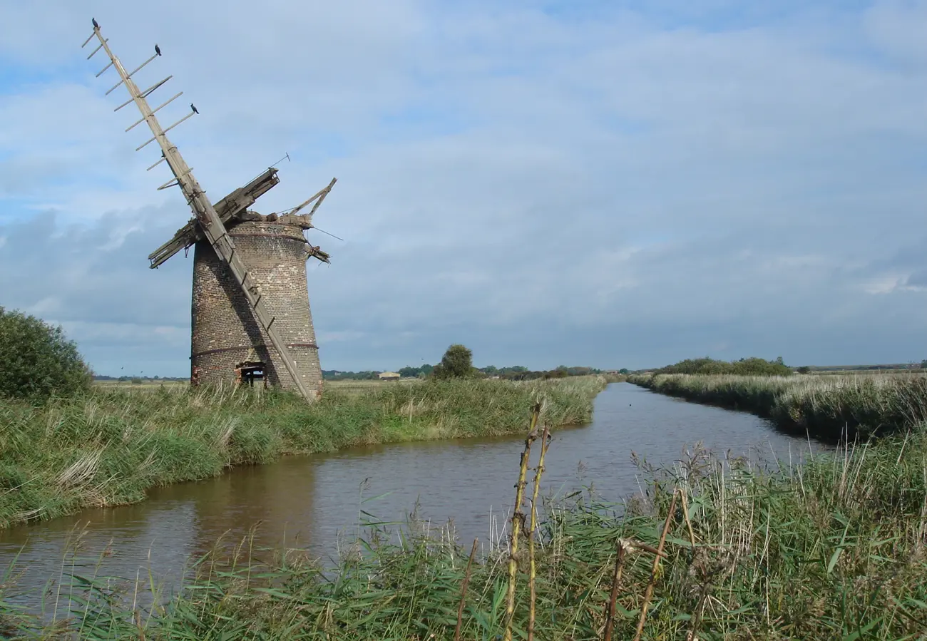 A disused windmill on the side of a river through the Norfolk Broads