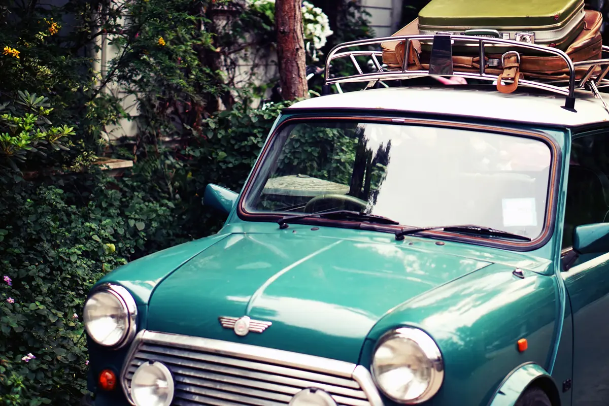 A classic turquoise Mini with luggage on its roof rack