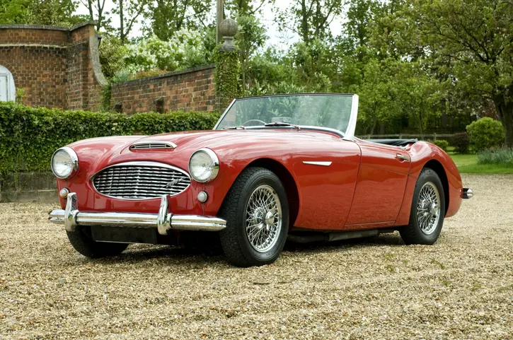 A red convertible Austin Healey parked on a gravel driveway